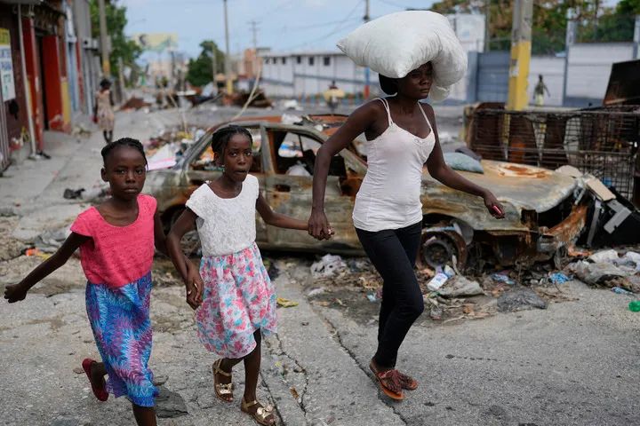 ▲5月2日，海地太子港民众在逃离家园时经过被烧毁的汽车。（美联社）