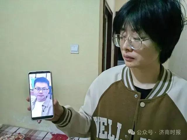 王龙妻子毛女士看着手机里的丈夫照片