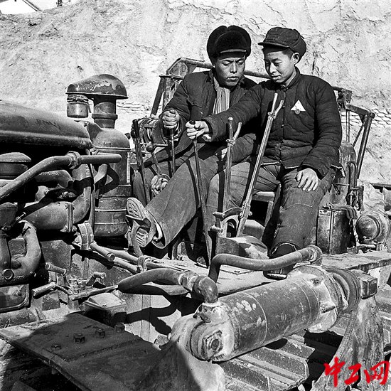 1954年，特等劳模郑福轩（左）在官厅水库工地教学员驾驶推土机。（工人日报资料图片）