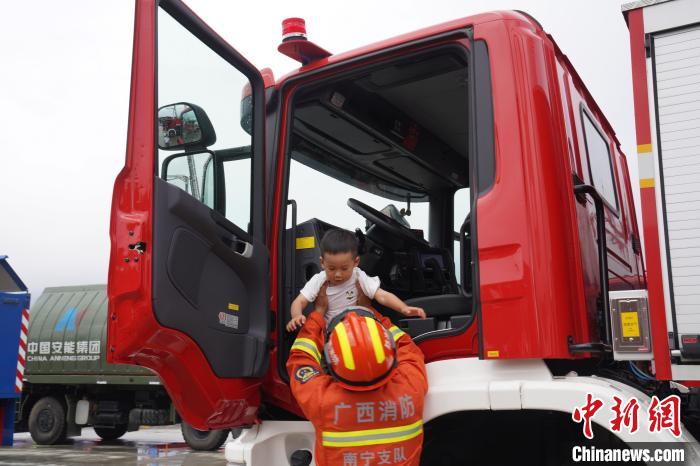 消防员将一位儿童抱上消防车驾驶位体验.