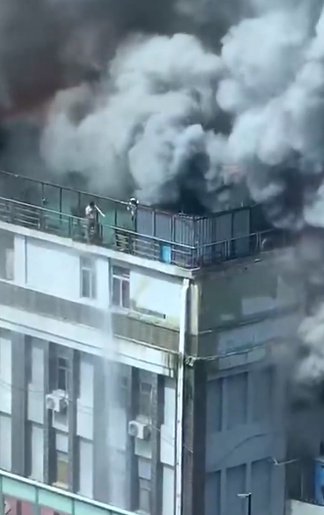 建筑上方浓烟滚滚，有人被困在楼顶上。 视频截图