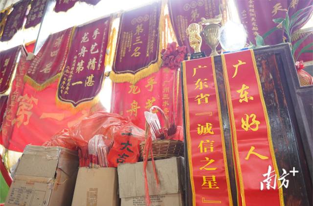 龙舟厂的墙上挂满了锦旗,还堆放着很多证书和奖杯.