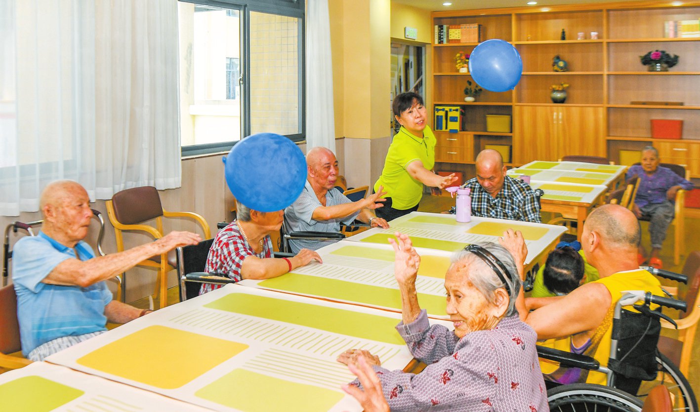在琼山区凤翔街道综合养老服务中心,工作人员在跟老人玩桌上拍球游戏.