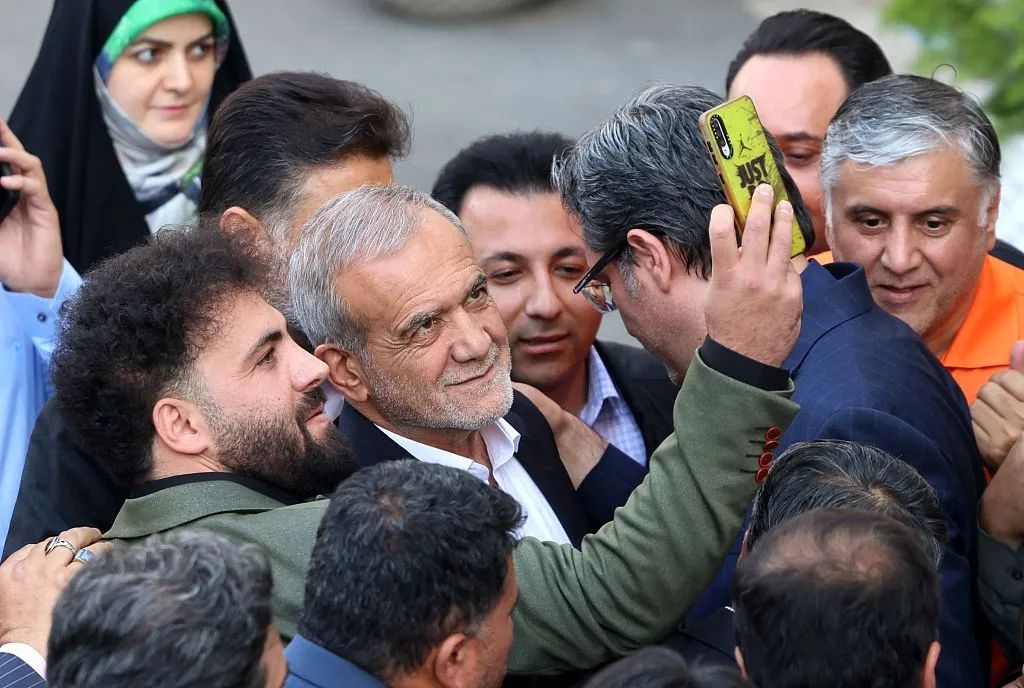 当地时间2024年6月18日，伊朗改革派候选人佩泽什基安（中）在德黑兰的一场竞选活动中与一名男子合影。图/视觉中国