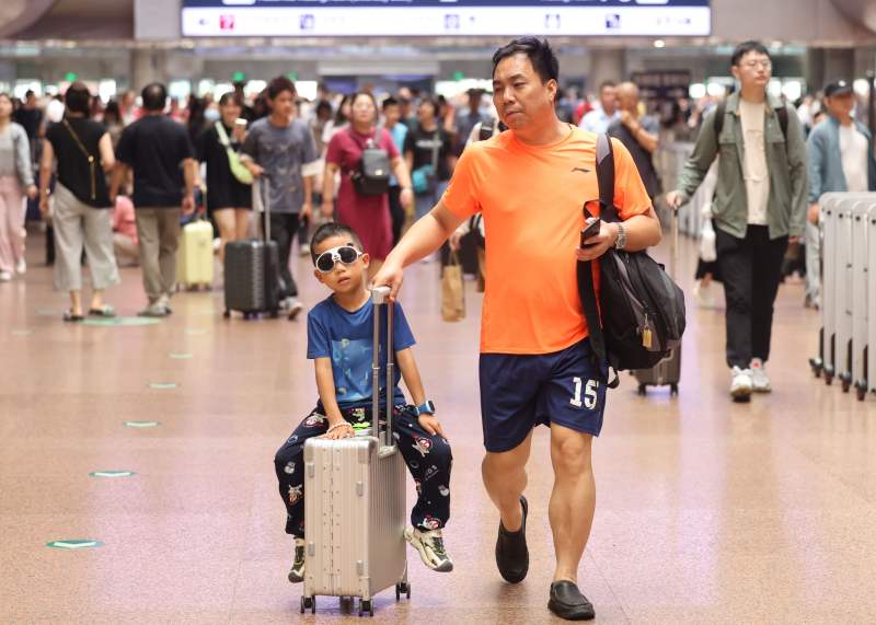 7月1日，北京西站，一位小旅客坐在行李箱上“滑行”。  新京报记者 王贵彬 摄