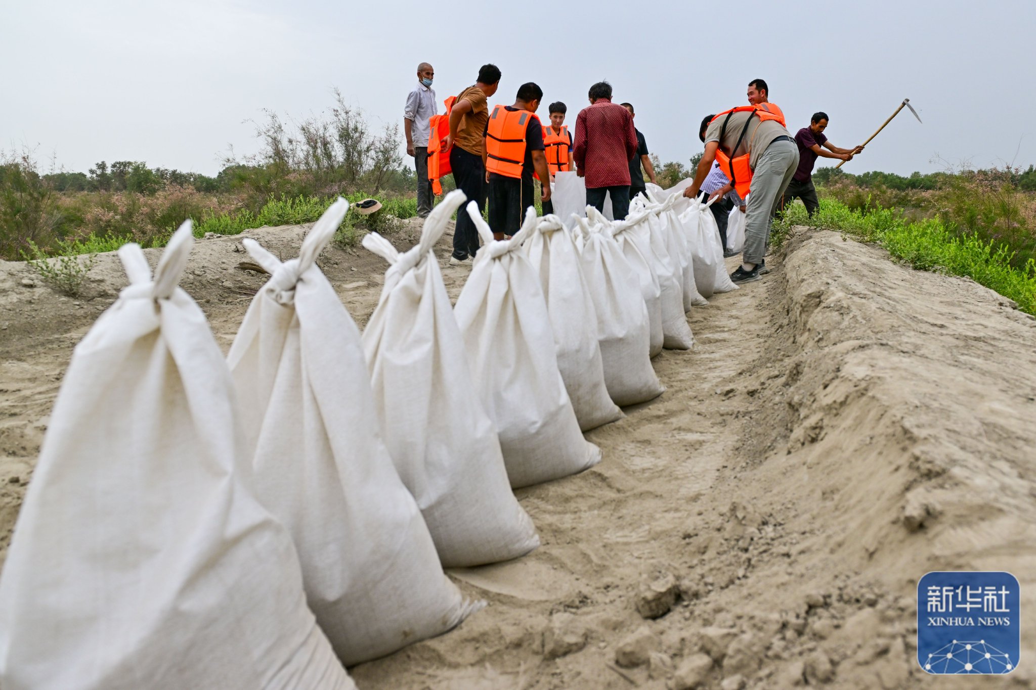 县盖孜库木乡一处河堤除险加固现场,抢险人员在装运沙袋(8月3日摄)