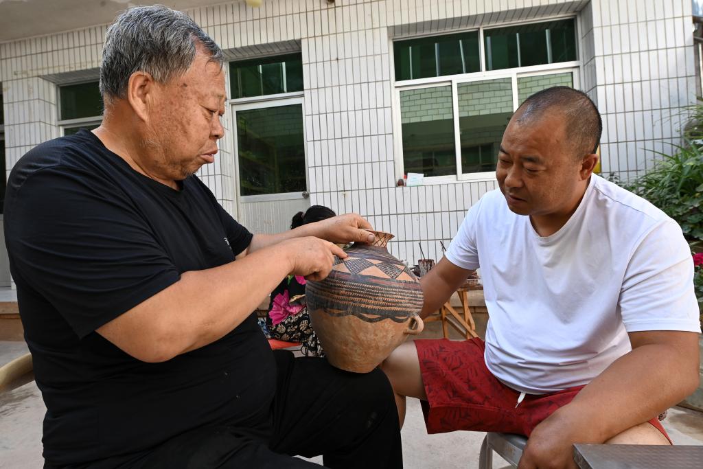 阎建林（左）在家中与儿子闫小虎探讨彩陶的线条。新华社记者 范培珅 摄