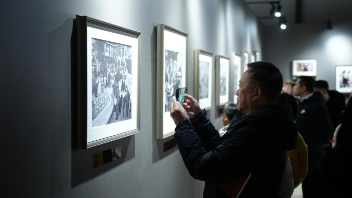 图为一位参观者正用手机拍摄着一幅1972年浙江杭州市民在菜市场选购副食品的老照片