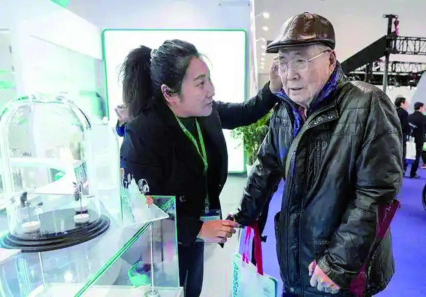 工作人员帮助一名参观者佩戴助听器产品 新华社发