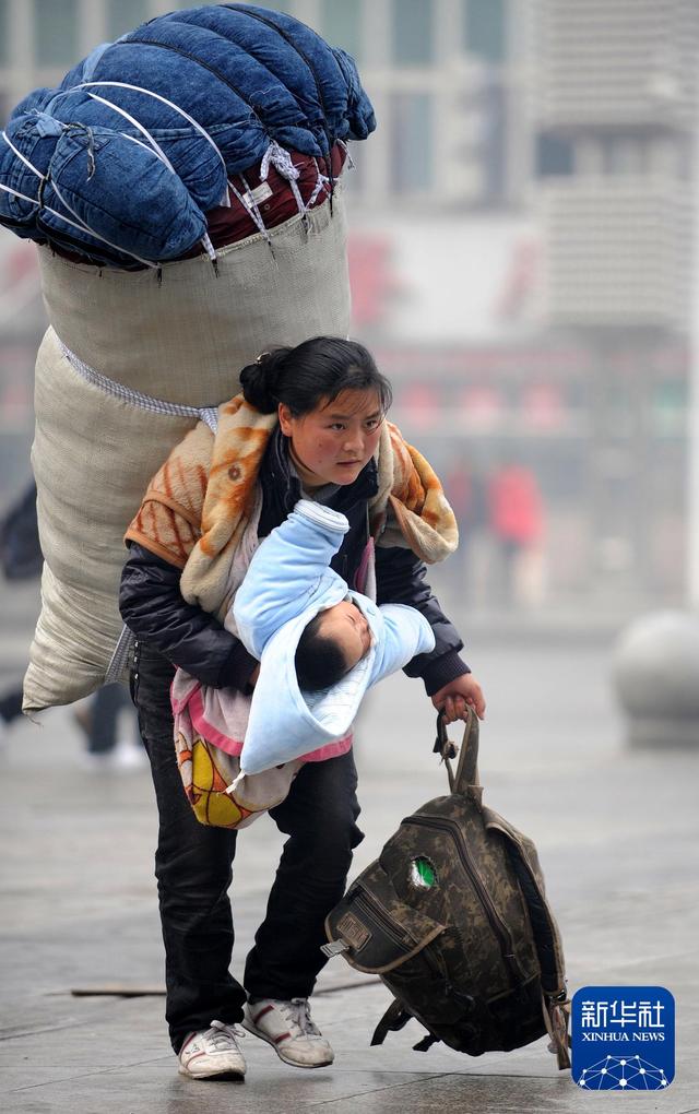 2010年1月30日，在江西南昌火车站，一位背负着超大行李的母亲怀抱孩子匆忙赶车。新华社记者 周科 摄