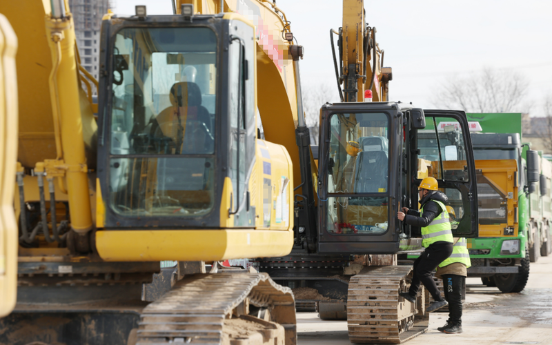 ▲资料图：某地一施工场所，施工人员登上挖掘机。新京报记者 陶冉 摄