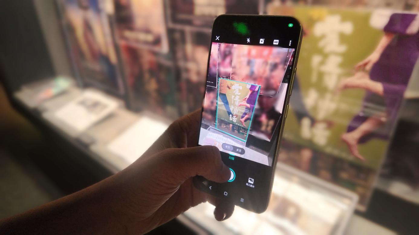 图说：参观者用扫描全能王App“智能高清滤镜”功能对《爱情神话》海报图像进行切边矫正