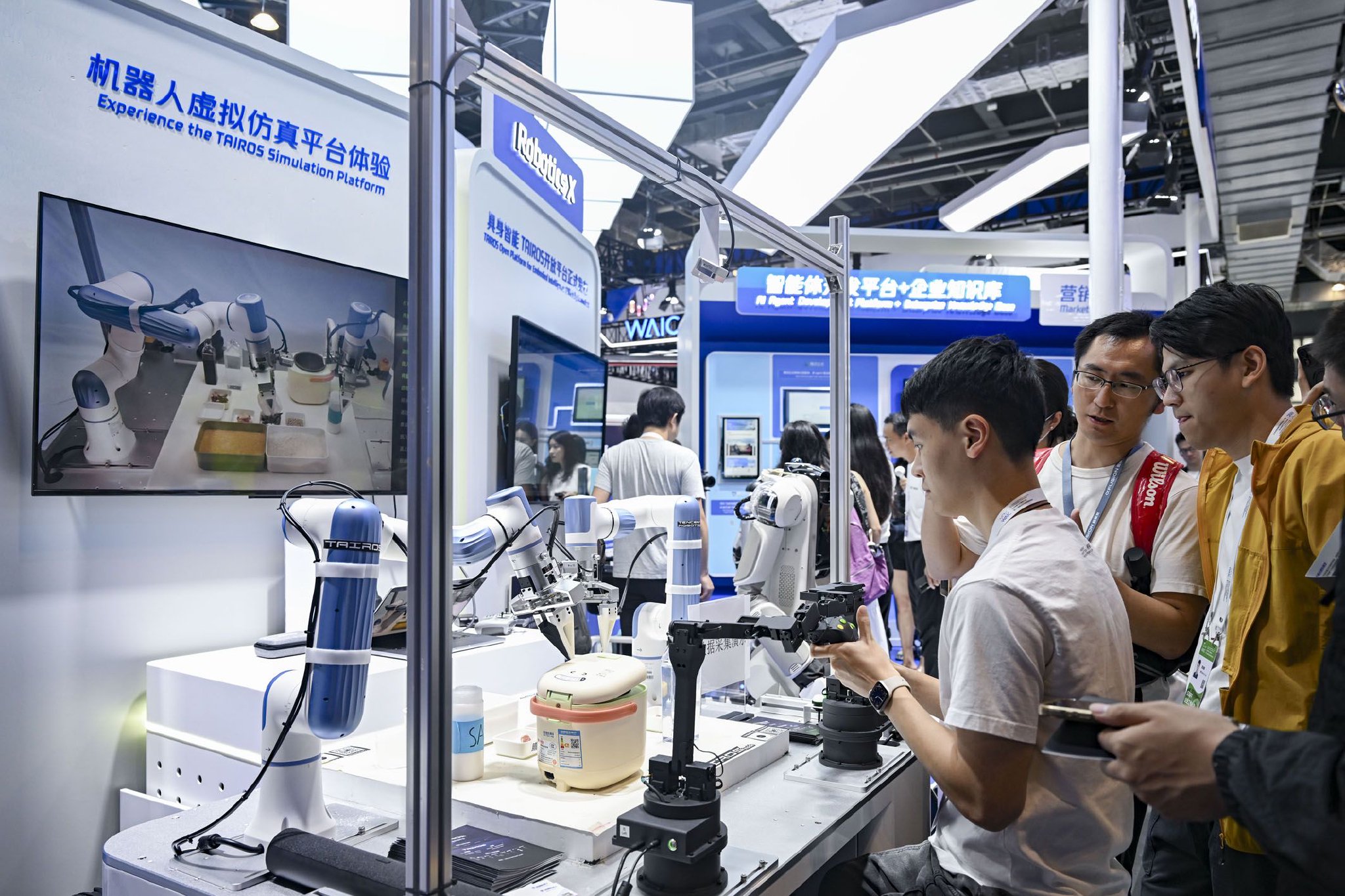 图为WAIC　2025上，展区工作人员（左）在向参观者展示具身智能开放平台。　　新华社记者　陈浩明　摄