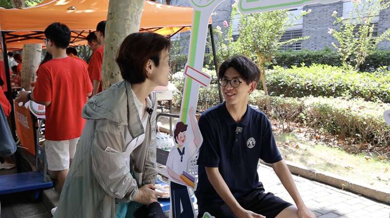 复旦哲学系学生志愿者常城在迎新摊位前指引学生拍照打卡。俞佳一/摄
