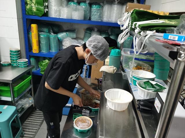 無堂食餐飲店的工作人員正在“做飯”——將標(biāo)準(zhǔn)化生產(chǎn)的“澆頭”拆包淋到飯上。 陳璽撼攝