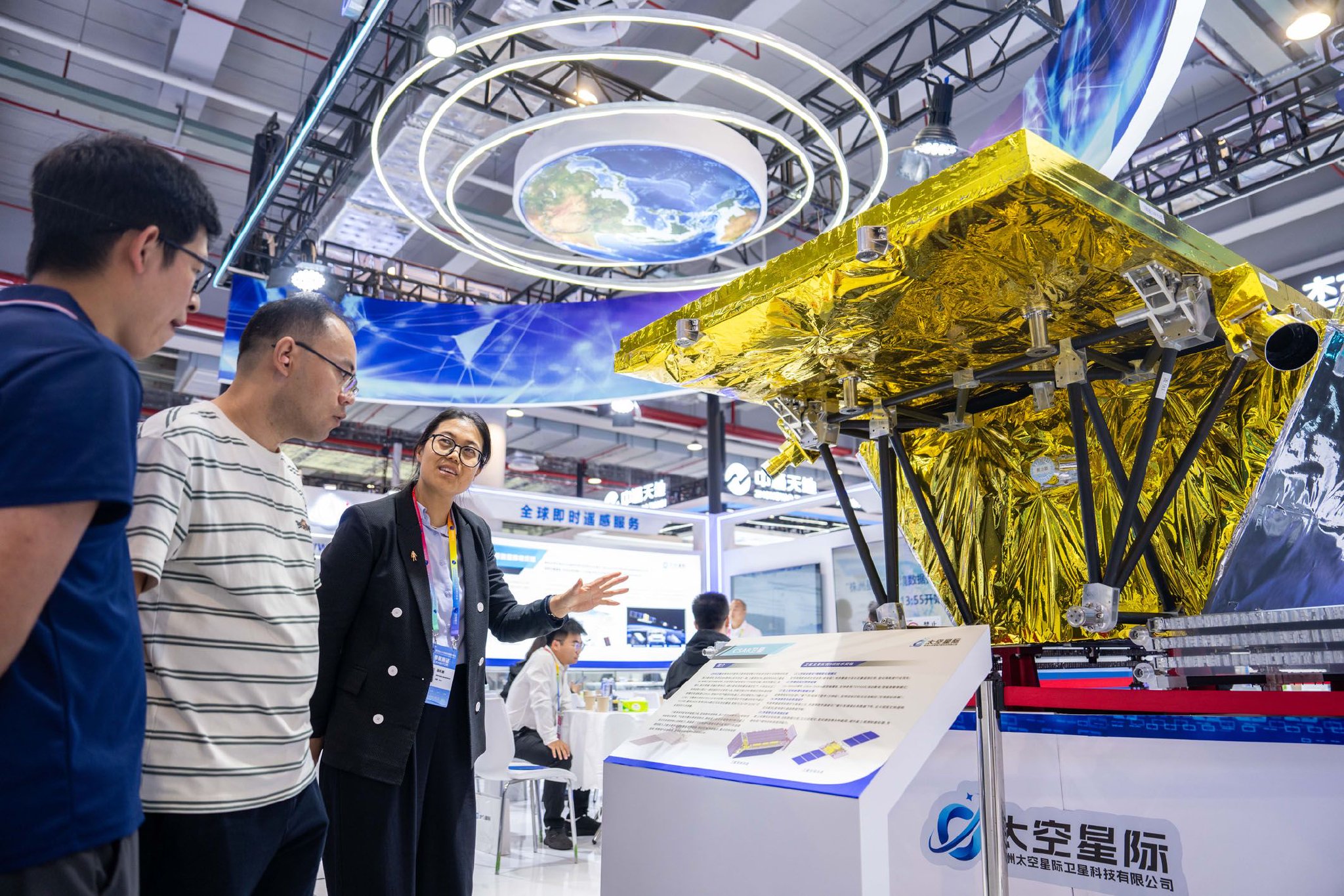 　　在湖南株洲国际会展中心举办的第四届北斗规模应用国际峰会上，工作人员（左三）在介绍一台对地观测卫星。新华社记者　陈思汗　摄
