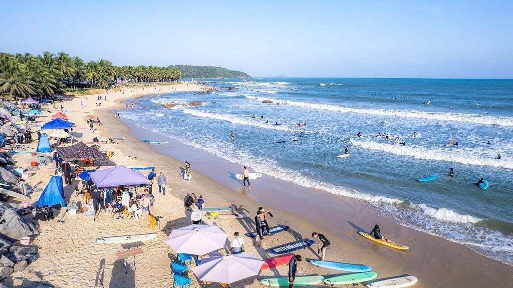 海南省万宁市日月湾阳光下的大海沙滩椰树以及在海面上冲浪。图/视觉中国