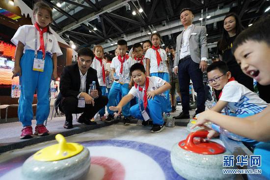 9月19日，小学生在冬博会一家参展商展区体验冰壶。