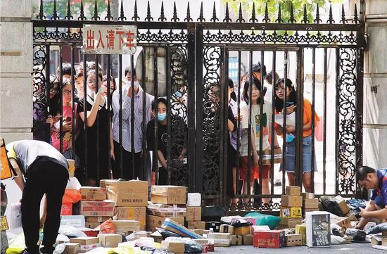 9月12日，河南郑州市一所大学校门前，学生们隔着栅栏门领取快递包裹。图/视觉中国
