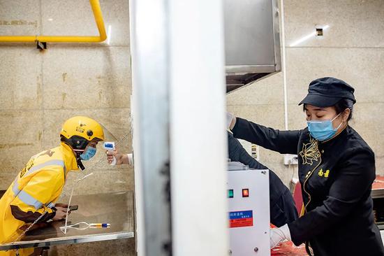 2月14日，湖南长沙市的一处外卖站点，外卖小哥赶来后首先做的是检测体温、酒精消毒，然后再取餐、外送。图/人民视觉