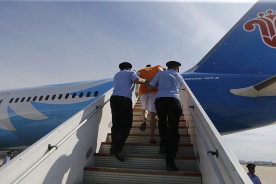 2019年8月28日，柬埔寨金边，民警每两人押着一名犯罪嫌疑人，登上飞机。（图/视觉中国）