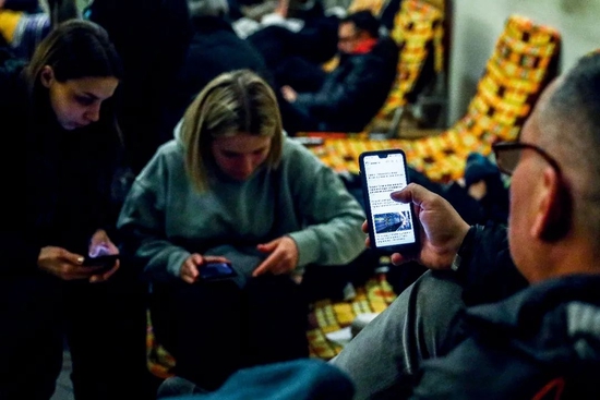 2月24日，乌克兰民众搭乘从乌克兰基辅开往波兰普热梅希尔的火车，期间在火车站一处临时避难所休息时，人们通过手机关注时事。图/人民视觉