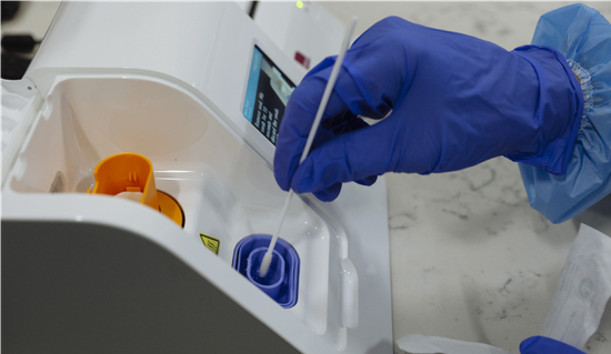 ■ 实验室技术人员将棉签插入新冠病毒快速检测仪器 / 盖蒂图片社 & Angus Mordant