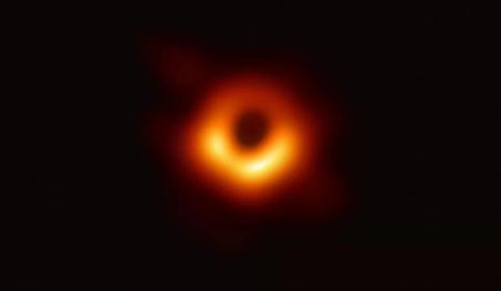 图1：M87星系中心超大质量黑洞（M87*）的图像，图中心的暗弱区域即为“黑洞阴影”，周围的环状不对称结构是由于强引力透镜效应和相对论性射束（beaming）效应所造成的。由于黑洞的旋转效应，图片上显示了上（北）下（南）的不对称性。