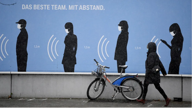在德国，一位女士走在一张海报旁边，上面写着“最佳团队、保持距离”。