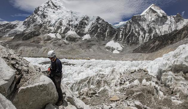 3、一位探险队成员正在珠峰大本营冰崖附近岩石上提取样本。