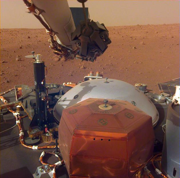 这是洞察号探测器机械臂上相机拍摄的图像，显示该探测器甲板上的仪器装置，背景是火星埃律西昂平原。这张照片拍摄于2018年12月4日。