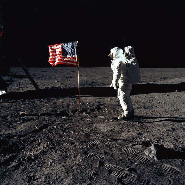 在这张由阿姆斯特朗拍摄的经典照片中，奥尔德林正在将美国国旗插上月球表面。注意前景中的脚印。这些宇航员留下的脚印至今仍清晰可见。