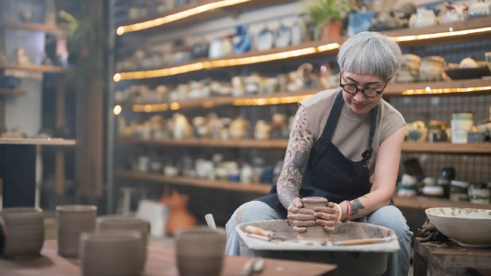 陶艺工作室里，一位老年女性匠人在陶轮上制作陶碗