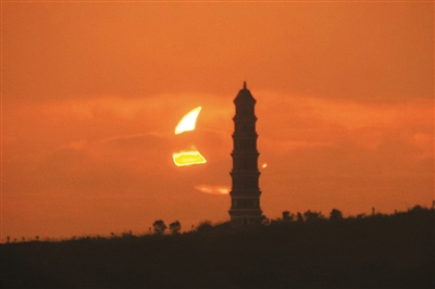 2012年5月21日，被蚕食得弯如金钩的太阳从广东省新丰县东郊的雁塔旁升起。潘慧恩摄