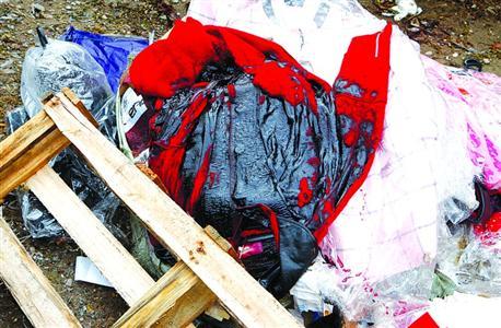 数十件被外漏化学品污染的崭新衣物堆在路边绿化带中，被腐蚀后，红色变成了墨黑色。晨报记者张佳琪