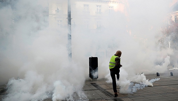 11月16日，法国南特，一名示威者踢走警方发射的催泪弹筒。图片来源：视觉中国