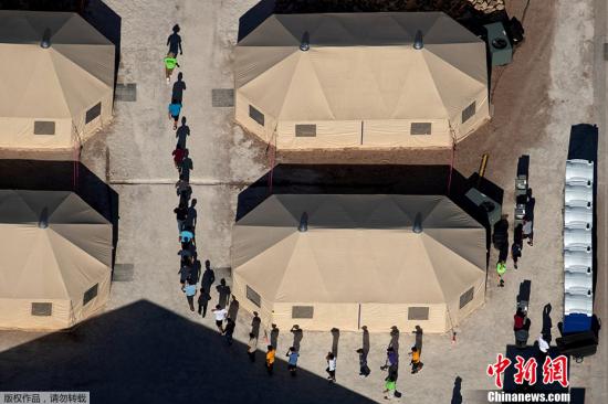 资料图：当地时间6月18日，美国德克萨斯州一所靠近墨西哥边境的拘留所里，与父母分离的移民儿童由工作人员带领排队穿行帐篷之间。MIKE BLAKE