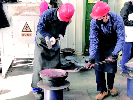 章丘铁匠在锻造铁锅。