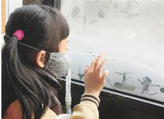 路公交车上,一名戴着便携空气净化装置的小学生正在车窗的哈气上作画
