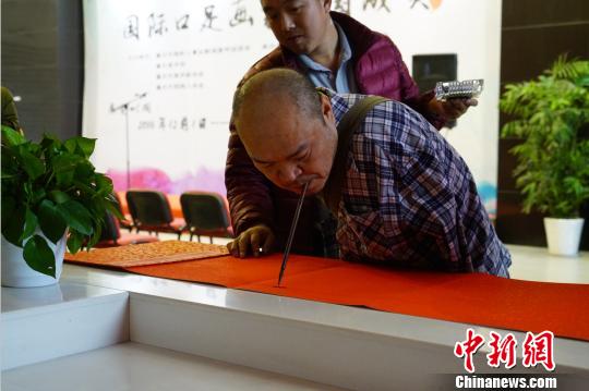 图为口足画家黄国富以口衔笔书写字画. 蒋青琳 摄