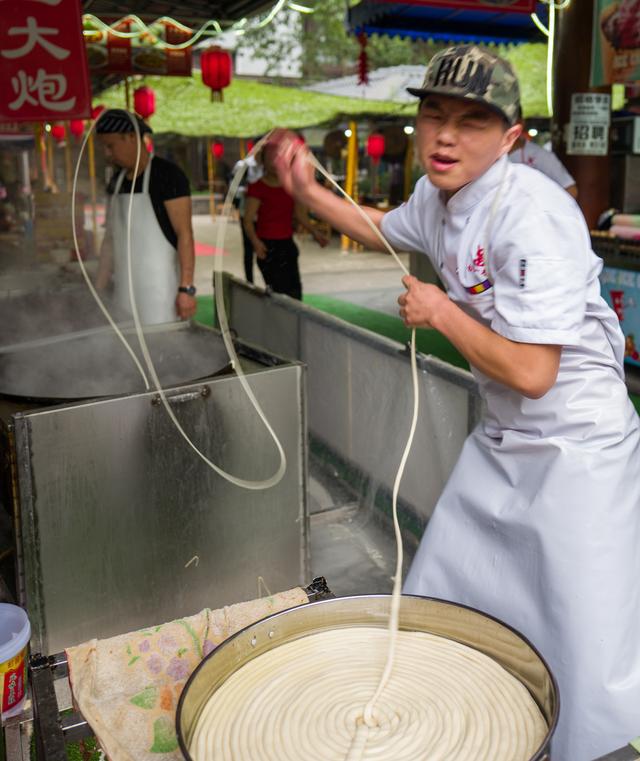 在成都黄龙溪古镇一家面馆前,一根面小哥摆出妖娆的动作和妩媚的