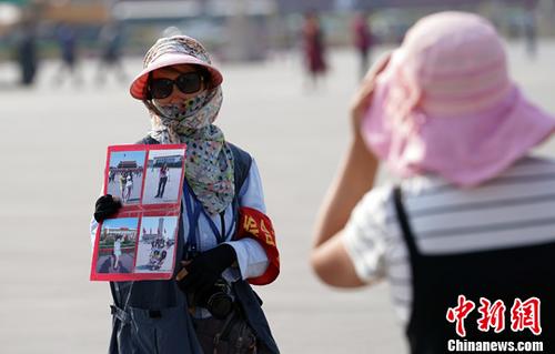 资料图：6月16日，一名天安门广场的照相师在高温天气中向游客推荐广场照相服务。中新社记者 毛建军 摄