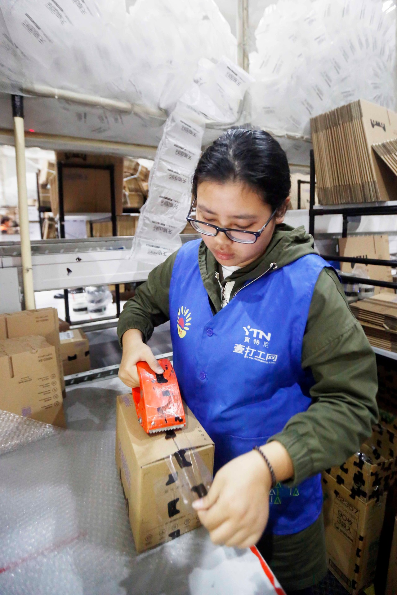 打包区的员工把消费者海淘的产品包装完毕,放入纸箱中,最后封箱.