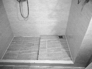 　曹女士家暖气管附近墙壁的裂缝。杨女士家沐浴区隔挡处高于卫生间整体平面十厘米。