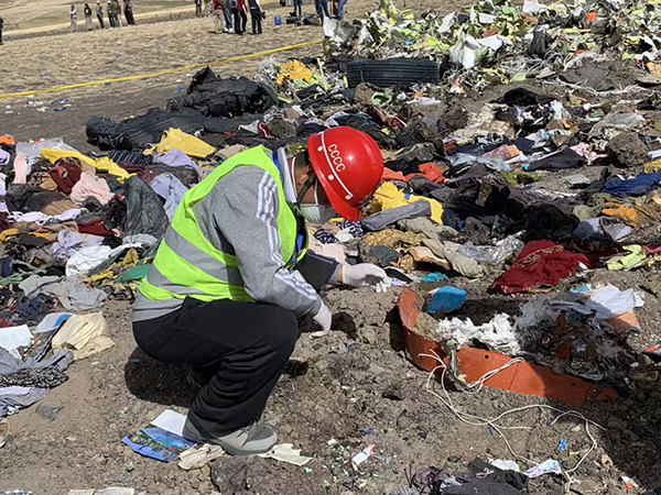 一名中国救援队员蹲在地上，周围散落着遇难者的衣物。