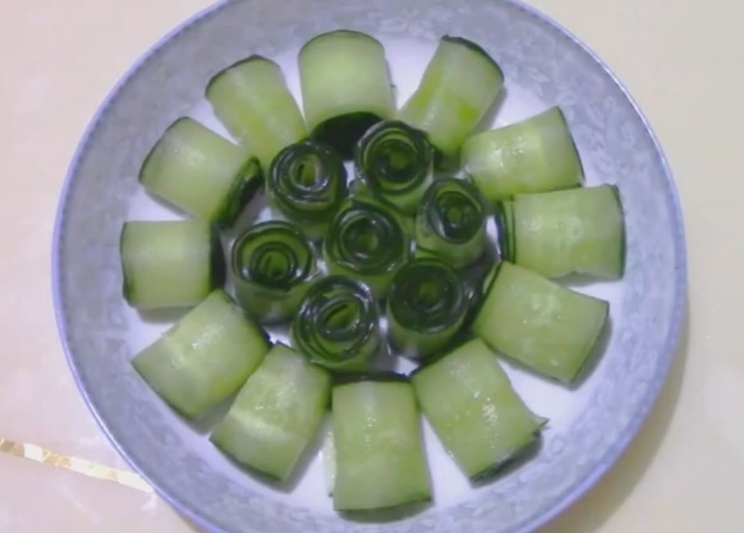 将黄瓜卷成卷后摆入盘中,中间竖着放,旁边的平着放.