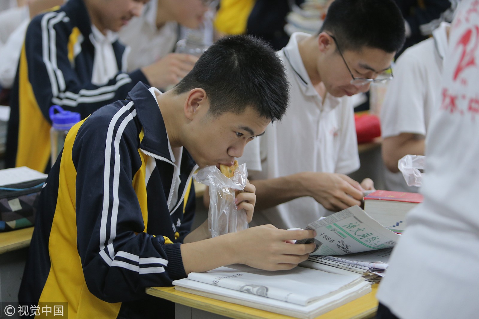 河北衡水二中晚自习前,一名高三学生边吃馅饼边看报纸学习.