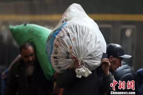 在南京火车站乘坐火车出行的旅客或扛或举或背着沉甸甸的行李准备上车。泱波 摄