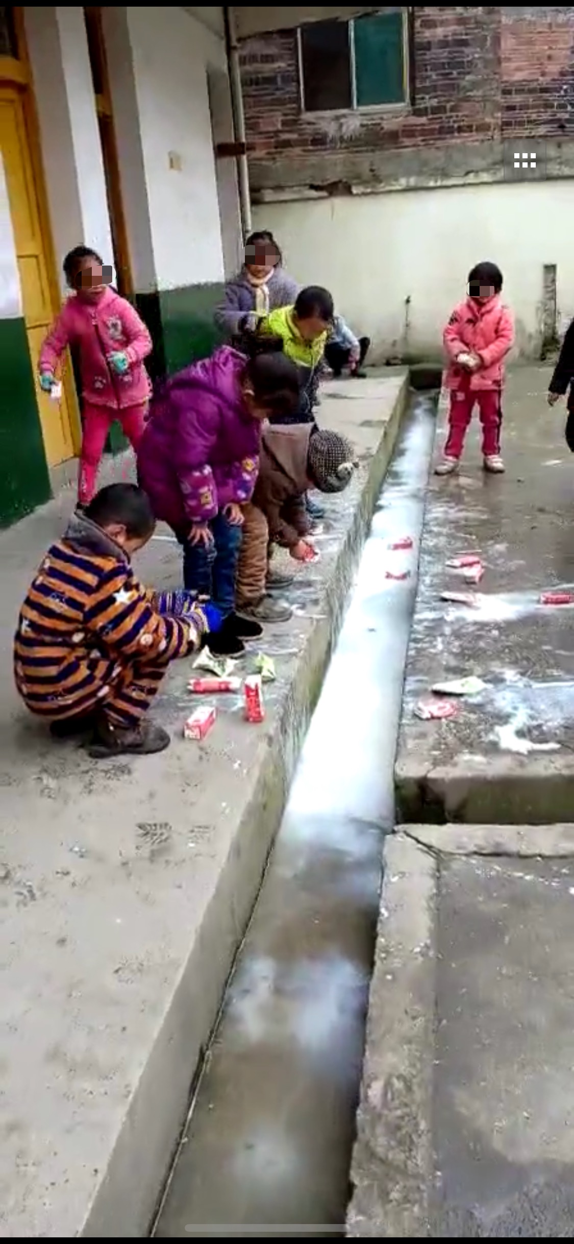 数名小学生蹲在教室外,将手中的牛奶倒入走廊边的水沟。来源:视频截图