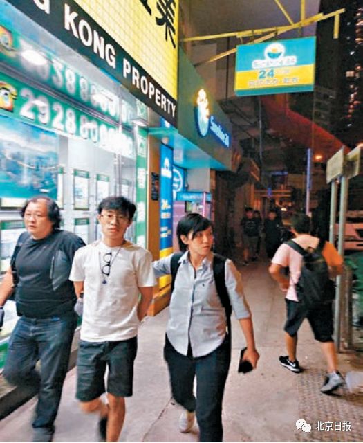 手机炸弹:狂徒用手机遥控炸弹袭港警 2人落网照片曝光(图) 其中一名涉案青年(白衫),由探员押解到大 角咀一单位搜证。来源:香港《文汇报》